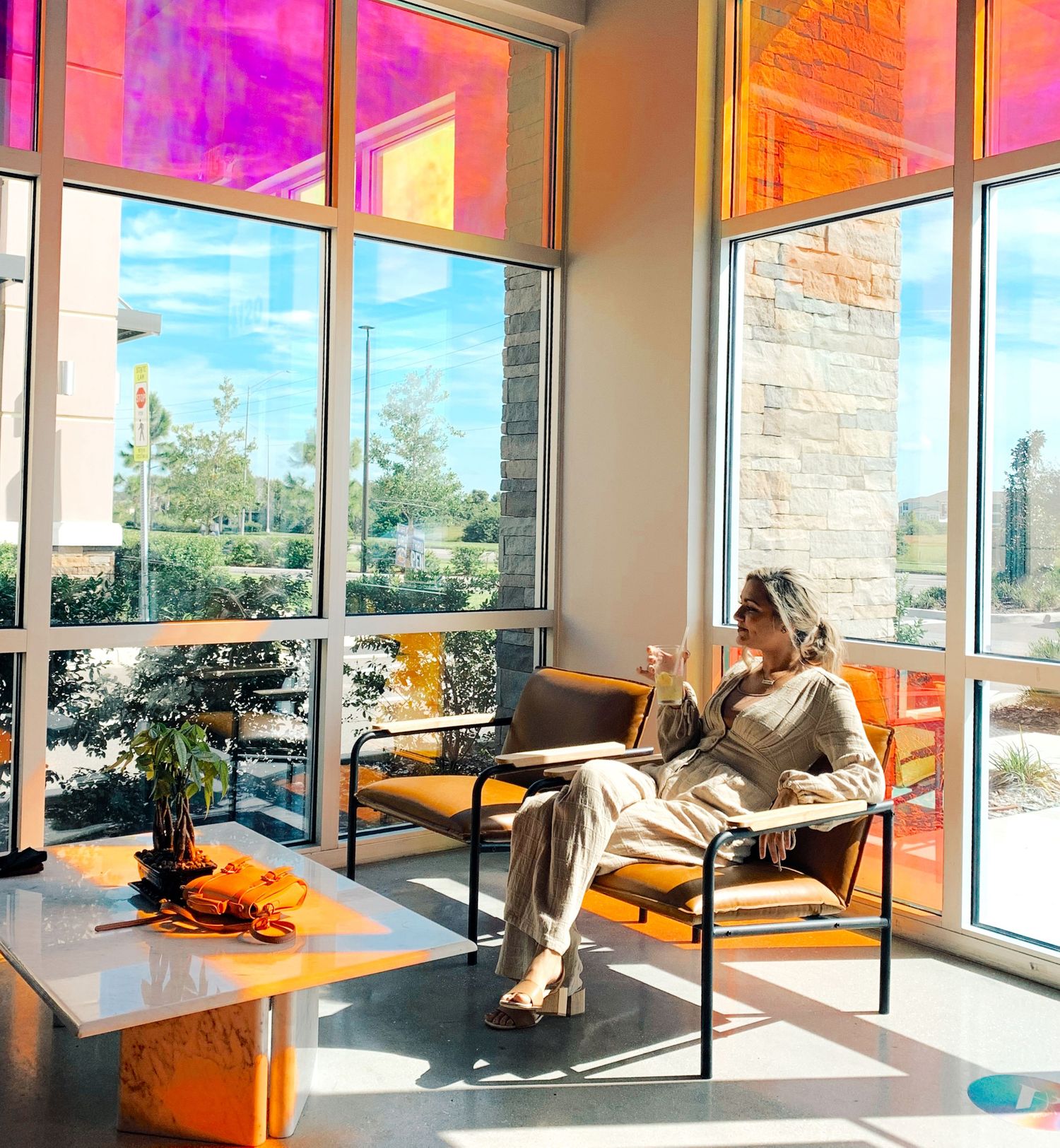 Sunlit corner with colorful window reflections and a person relaxing in a modern lounge chair.