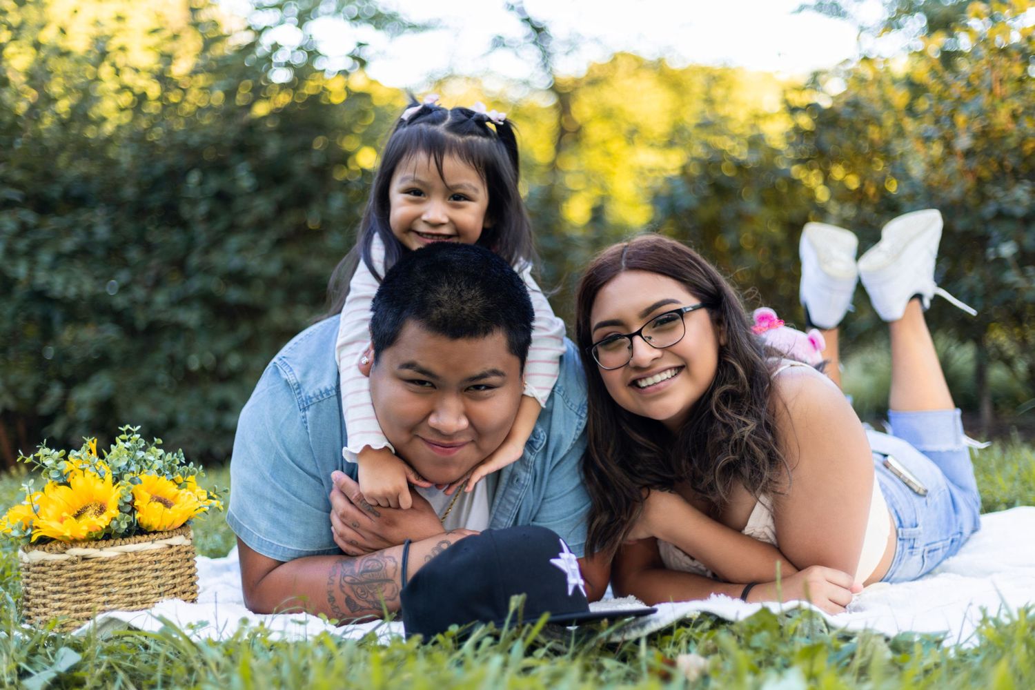 Family lying on picnic blanket in park during golden hour.
