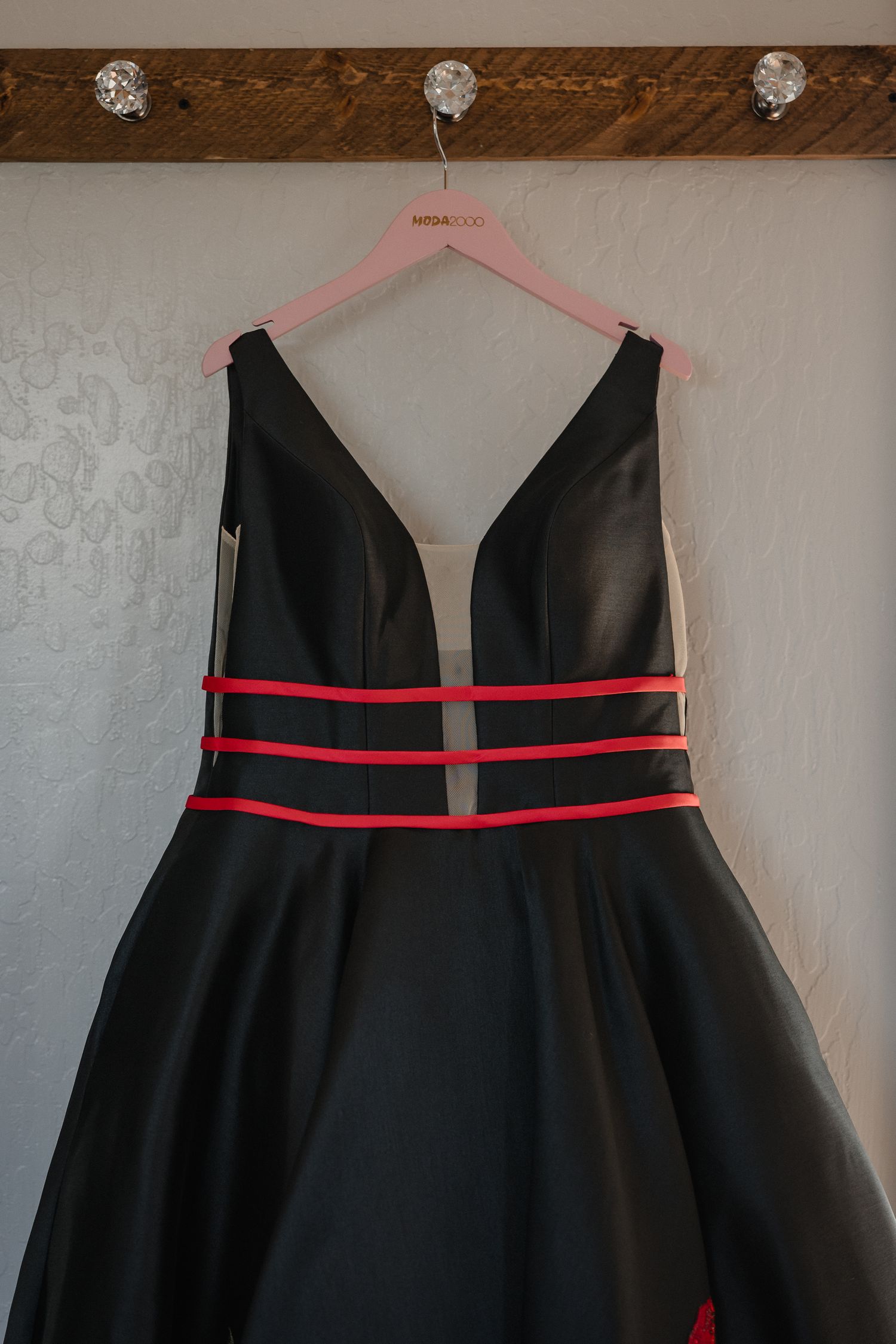 Elegant black formal dress with red stripes hanging on pink hanger against white wall.
