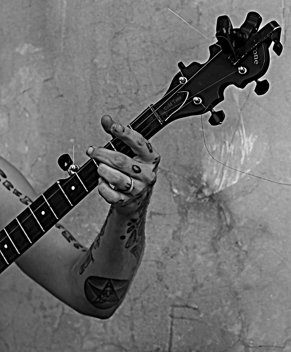 Close-up black and white shot of a tattooed arm holding the neck of a bass guitar.