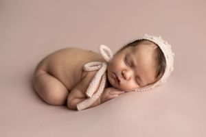 newborn baby girl laying on side on top of pink background with pink knit bonnet