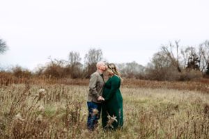expecting couple embracing in field with mom in green gown