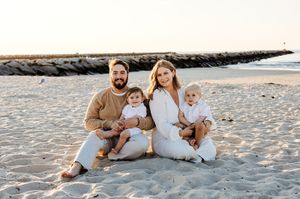 family of four sitting at sunset on the beach at low tide