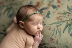 bird's eye view newborn baby girl laying on green flowered background with green bow headband