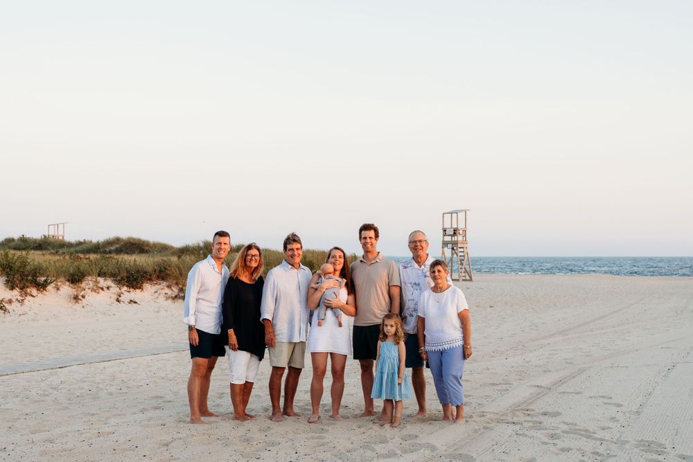 A group poses for a casual beach photo at dusk with the ocean visible in the background.