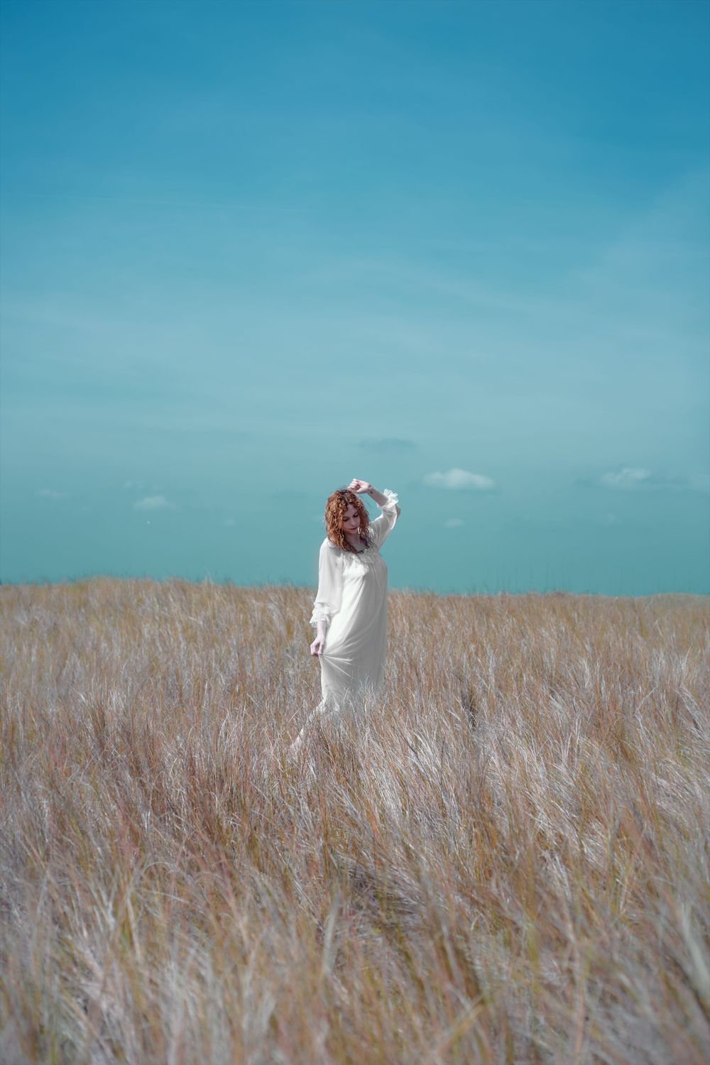 A Woman in white standing in the middle of a field under a teal sky.