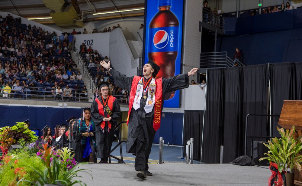 Graduate celebrates enthusiastically on stage during commencement ceremony.