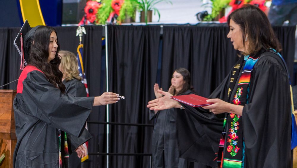 Graduates in black robes and red stoles exchange documents during ceremony.