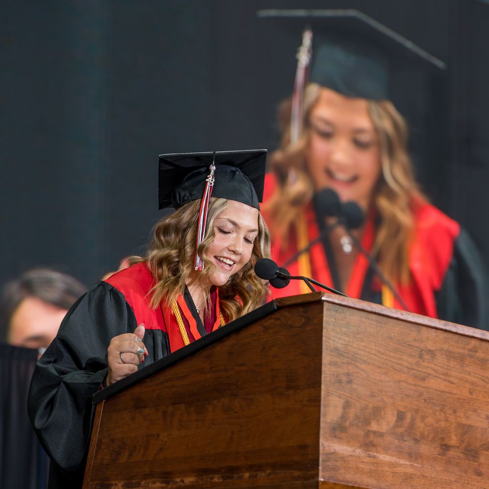 Graduate smiles while reading speech at wooden podium during ceremony.