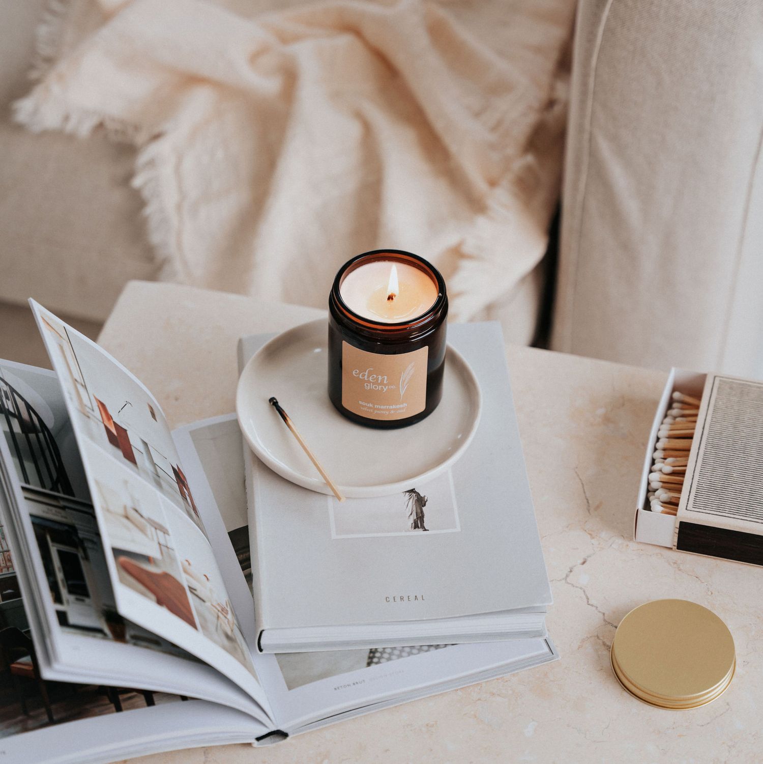 A minimalist flat lay of open books and a candle on a light beige surface.