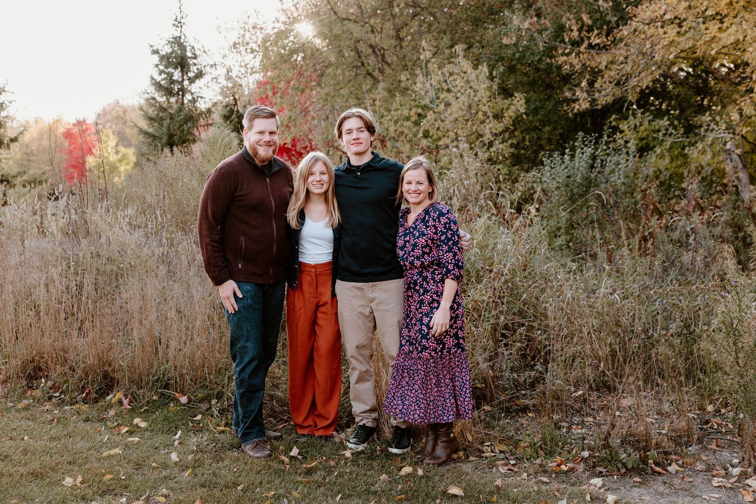 A group of people stands together outdoors during autumn with trees in the background.
