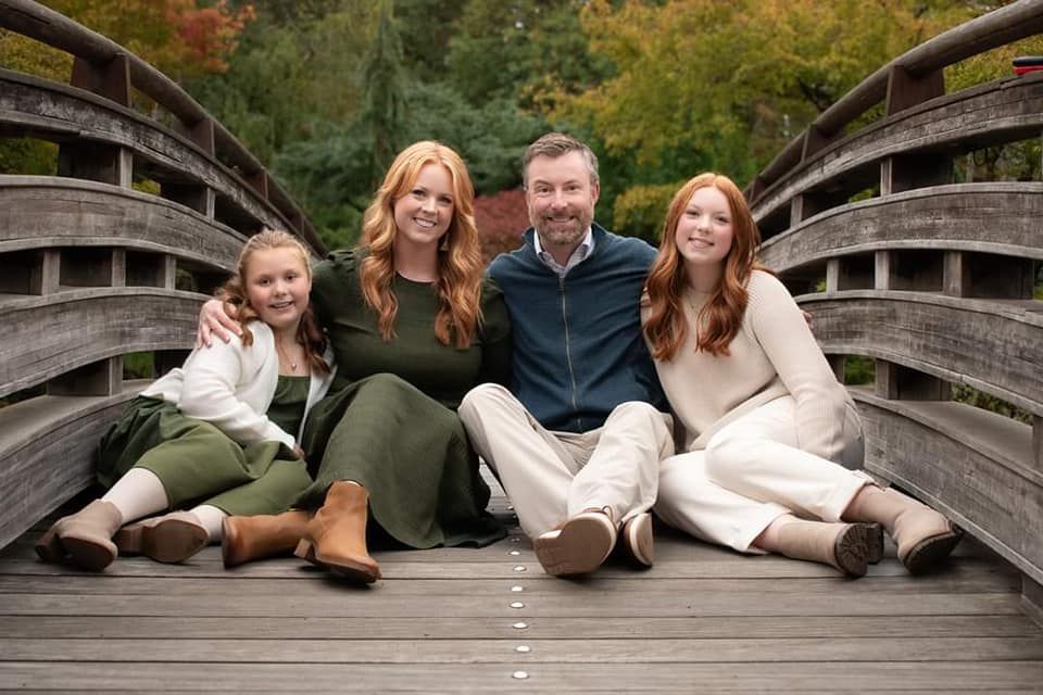 Four people sitting together casually on a wooden bridge in fall weather wearing cozy sweaters.
