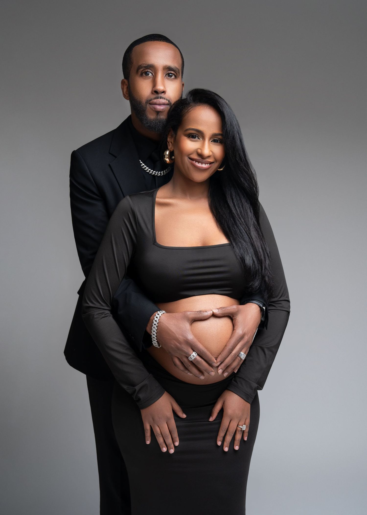 an expecting couple stand together with his hands around her belly for their studio maternity photo shoot