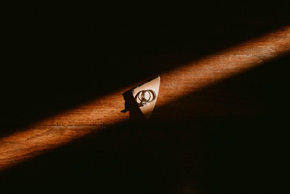 Wedding rings illuminated by dramatic lighting on wooden surface.
