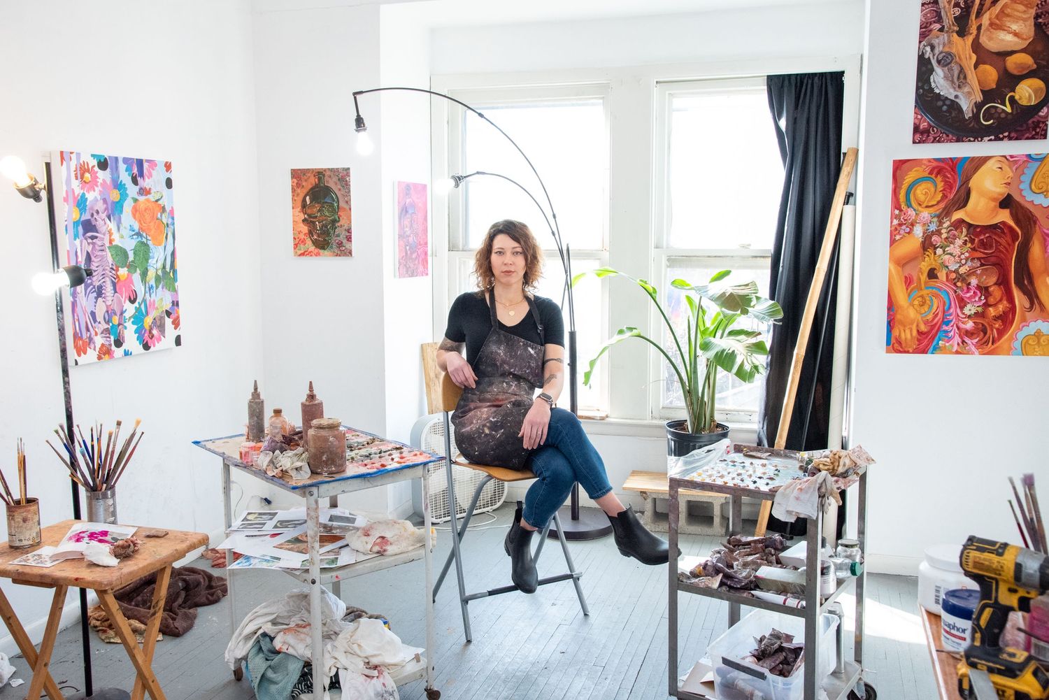 Bright white artist studio space with multiple paintings displayed on walls and easels.