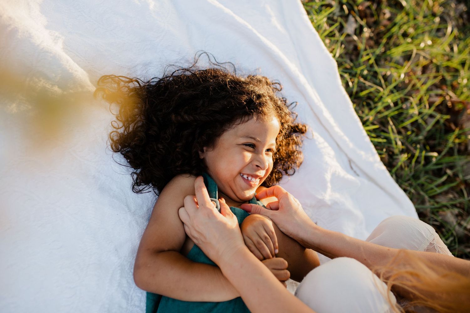 A joyful child with curly hair laughs while wrapped in a white sheet outdoors.