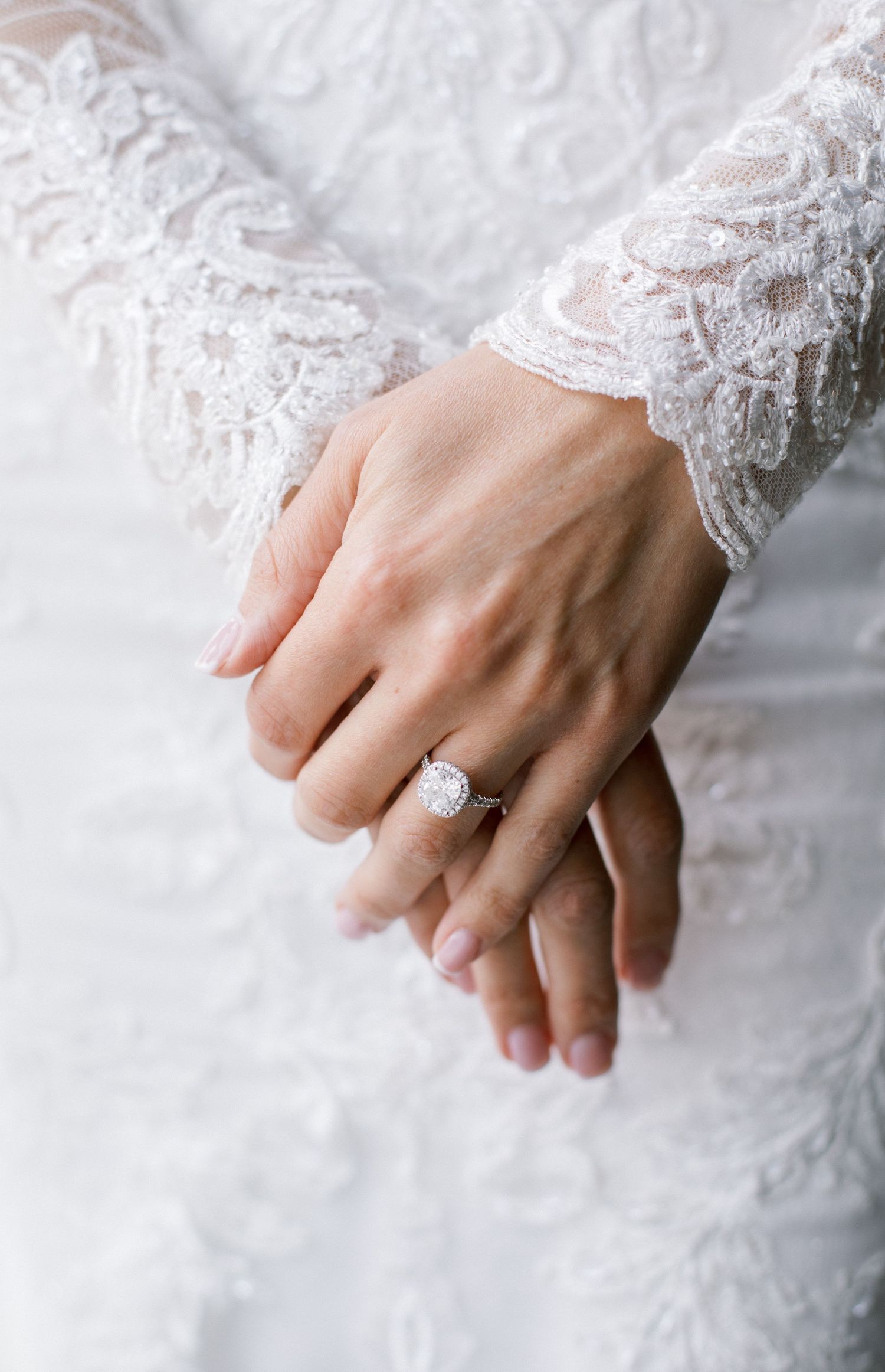 Close-up of delicate lace sleeve and engagement ring on woman's hand.