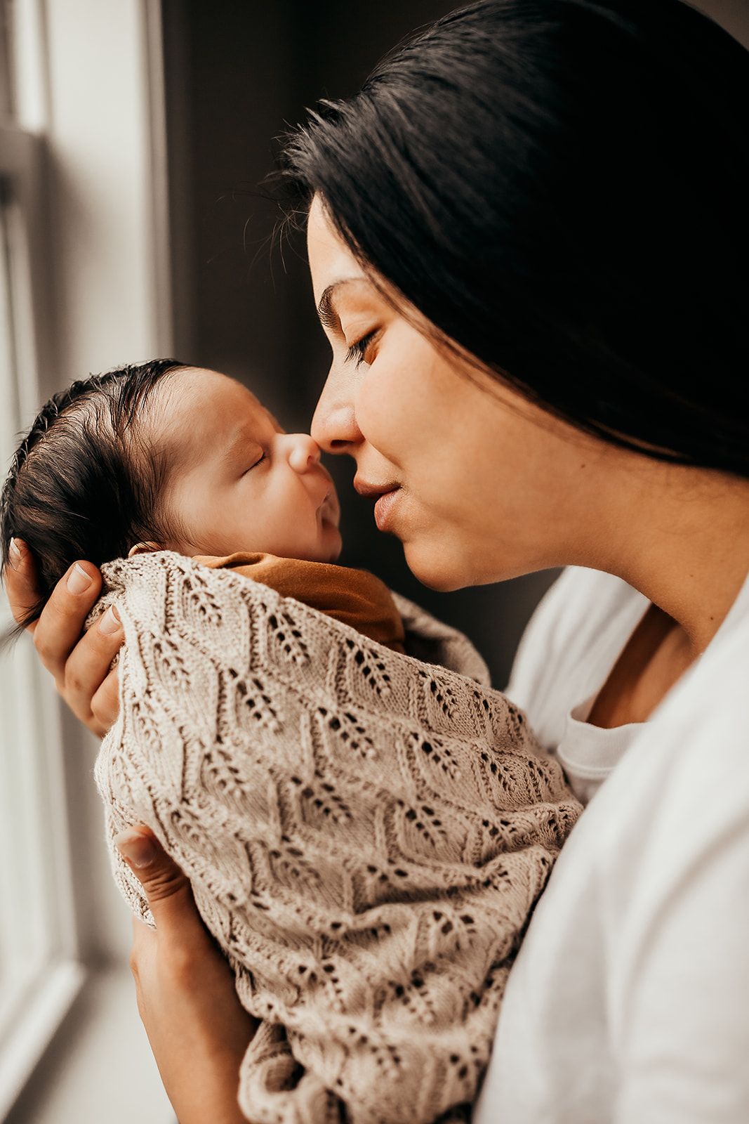 A mother holds her baby up to give him Eskimo kisses during and Oahu In Home Newborn Photoshoot.