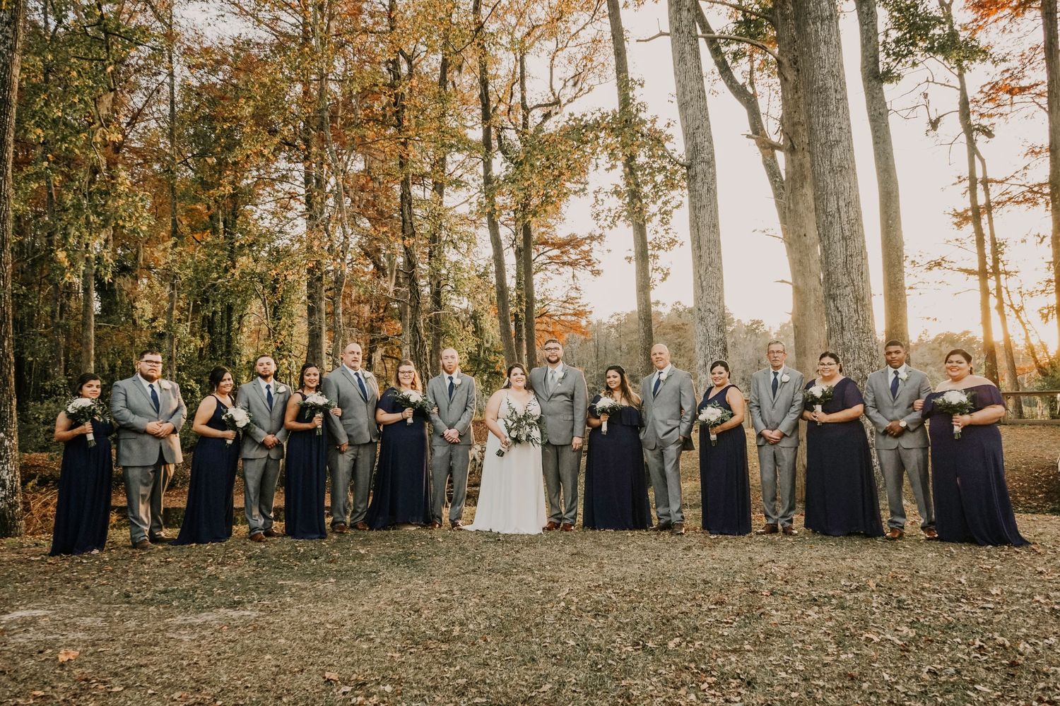 Wedding party in navy blue dresses stands in a line against autumn trees.