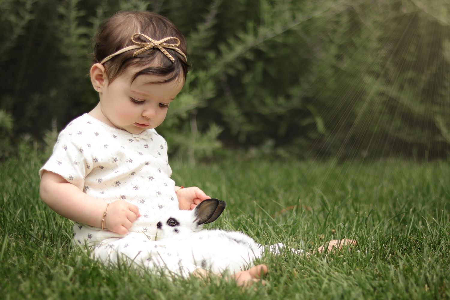 toddler sitting in the grass looking at her fluffy pet bunny