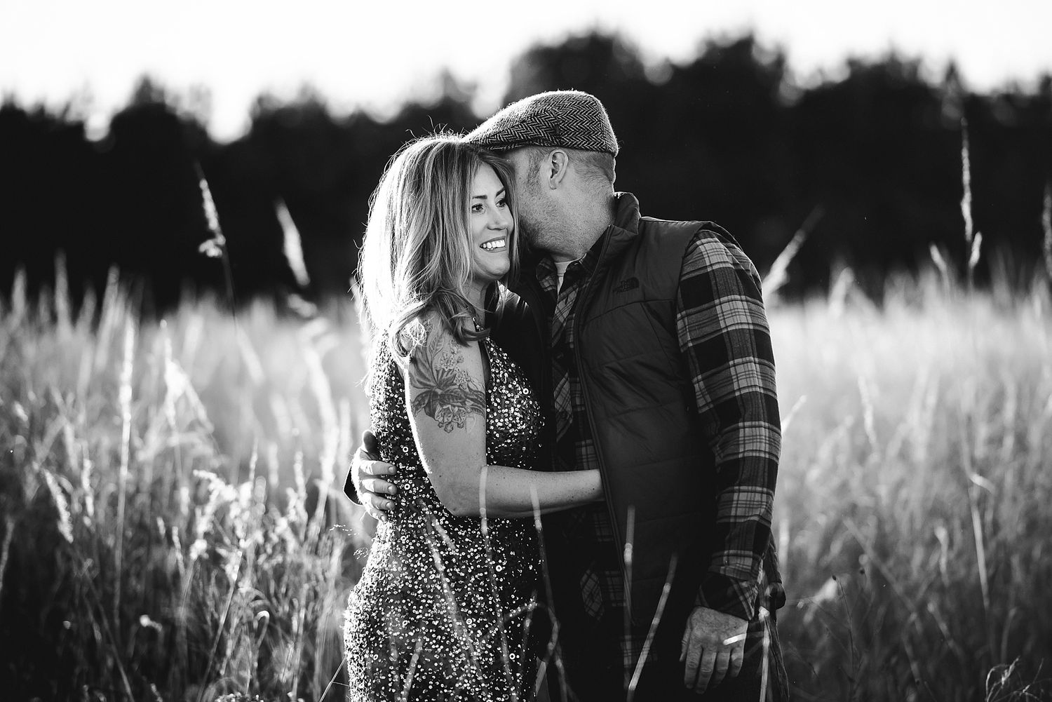 A couple embraces in a sun-lit field of tall grass at golden hour.