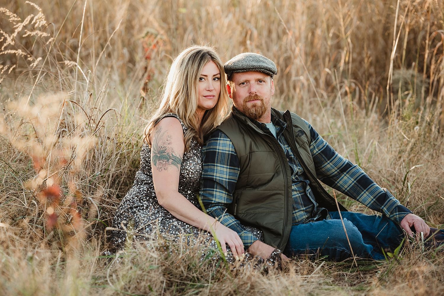 A couple sits together in a rustic fall setting among tall grasses at sunset.