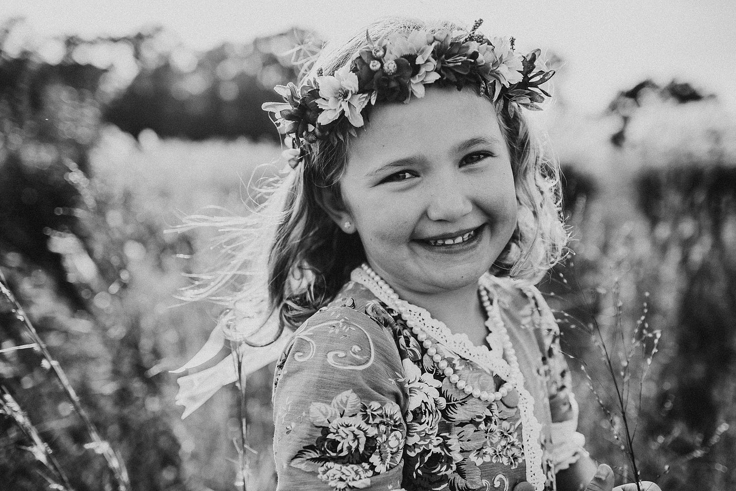 A black and white portrait of joy wearing a floral crown in a meadow.