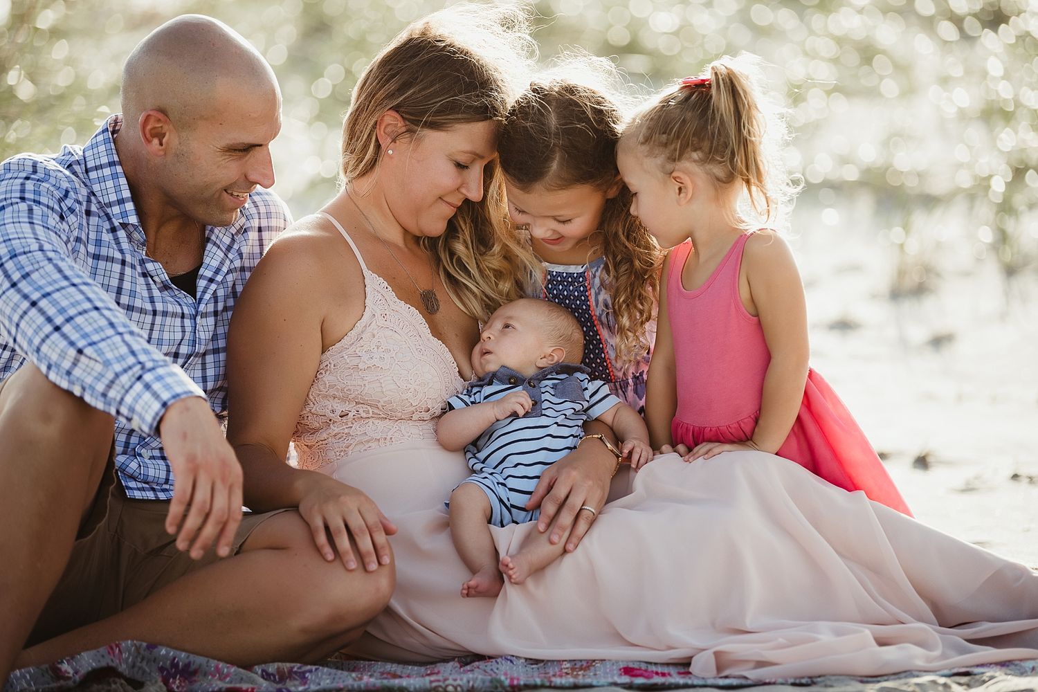 Family sitting together on beach sand sharing special moment with newborn baby.
