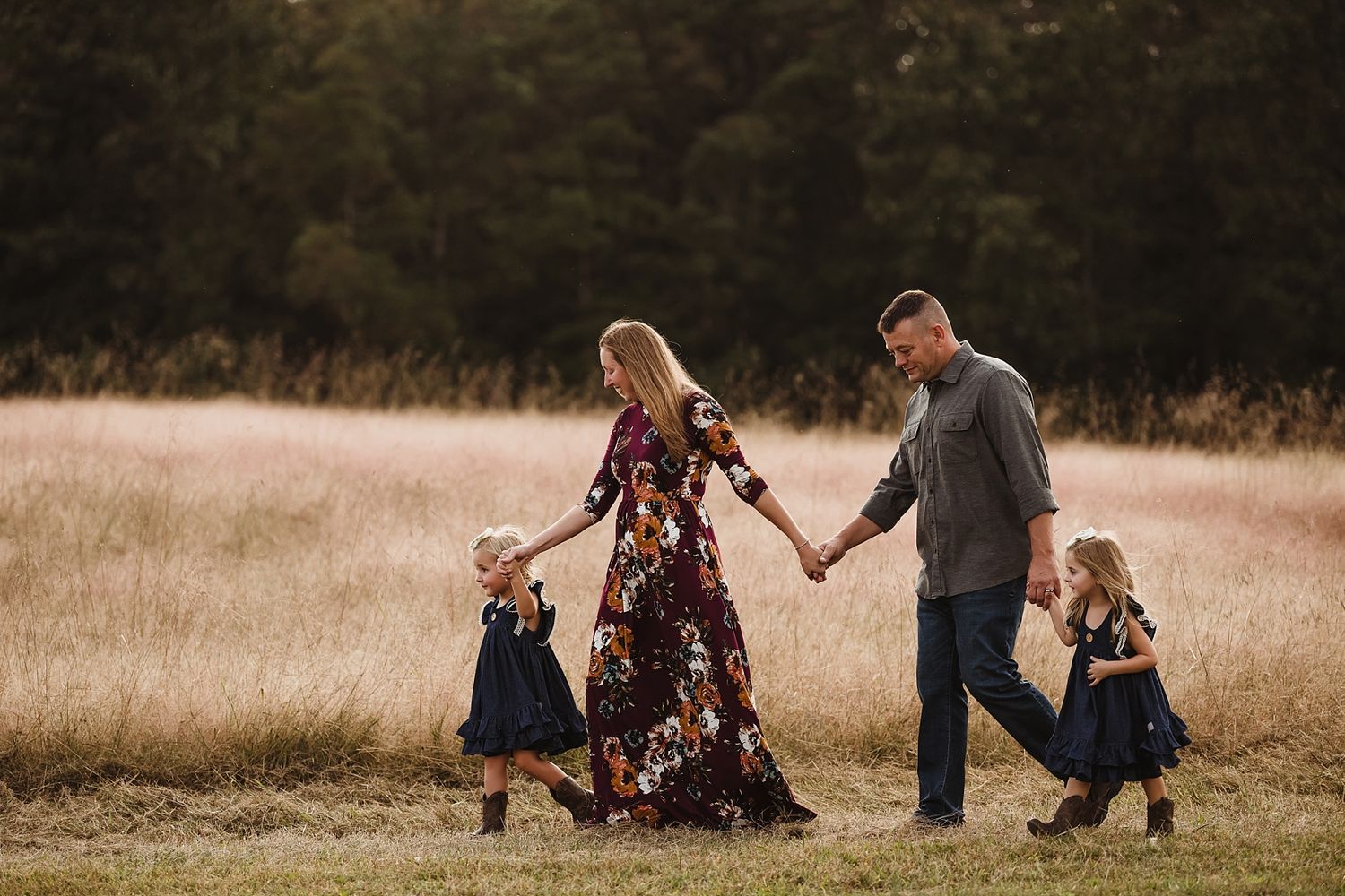 Family walking hand in hand through golden field at sunset.