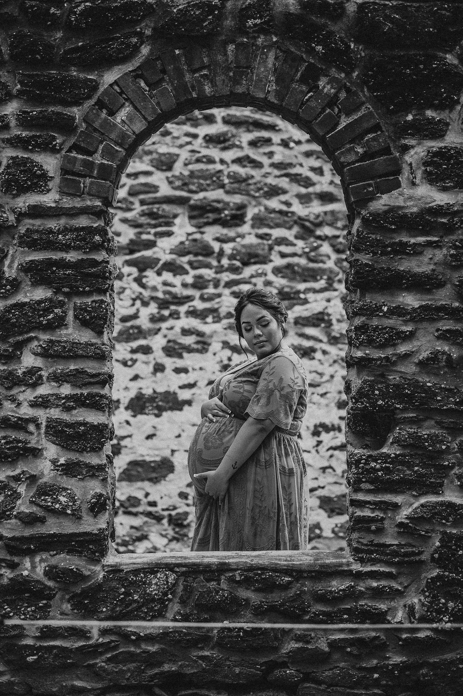 Dramatic black and white maternity portrait framed within stone archway.