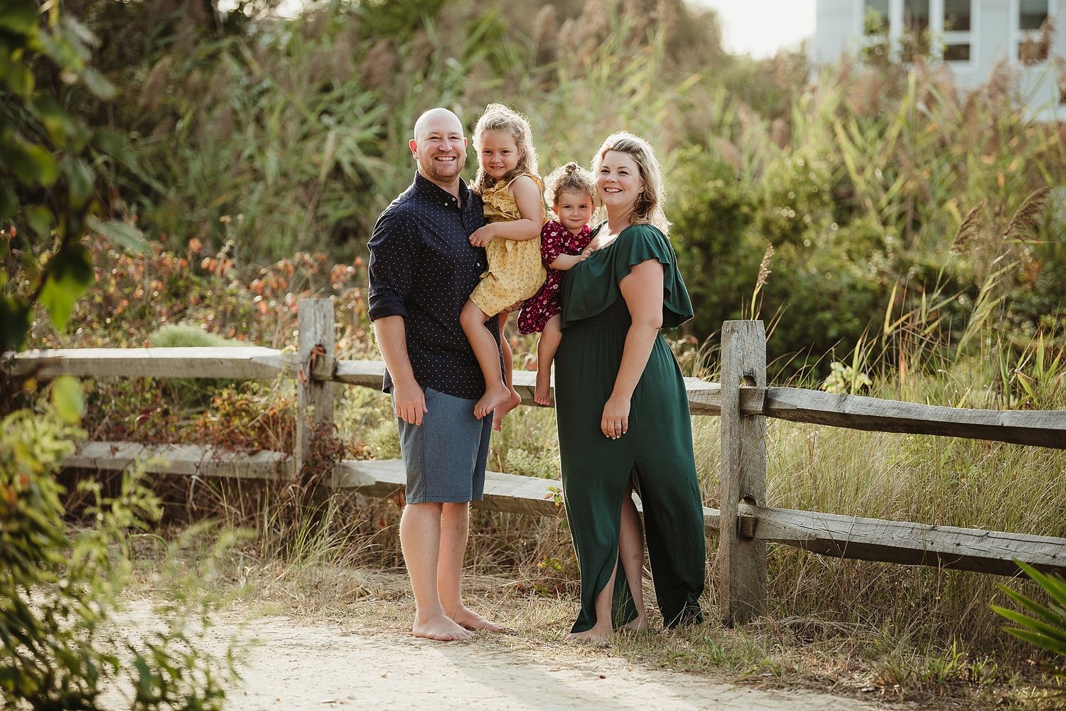 Family portrait on sandy path with natural coastal vegetation in background.