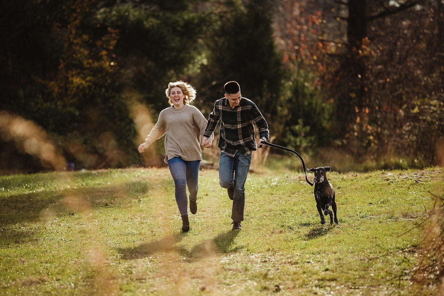 Couple and their black dog joyfully running together through a sunlit autumn meadow.