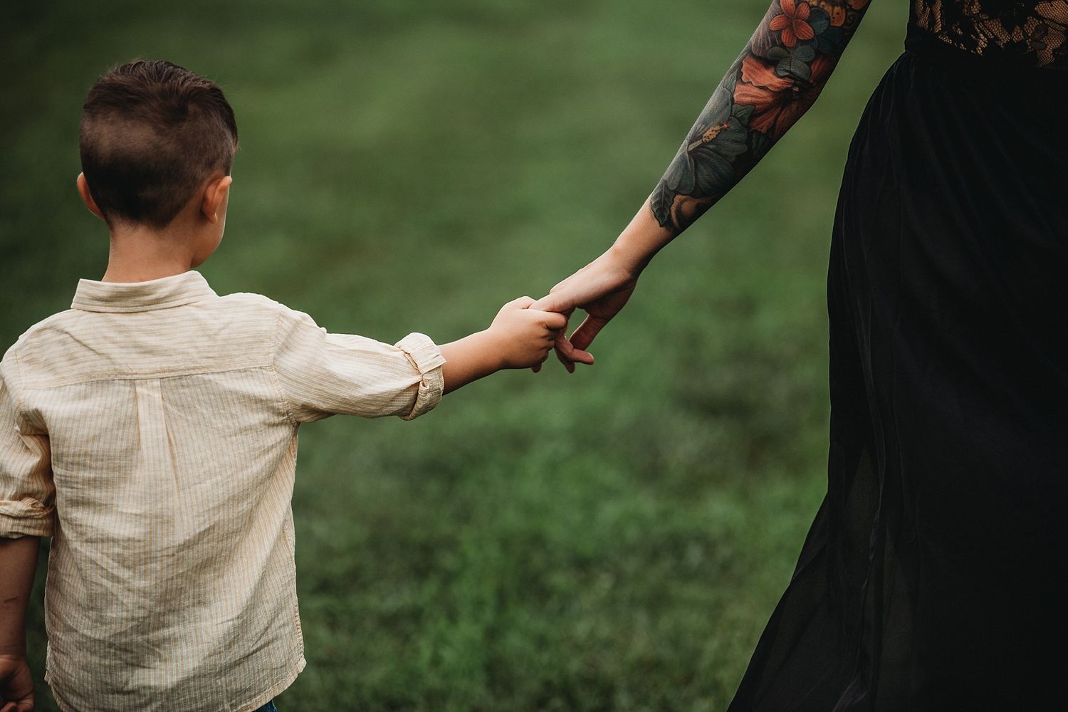 Close-up of tattooed arm holding hands in an emotional outdoor moment.