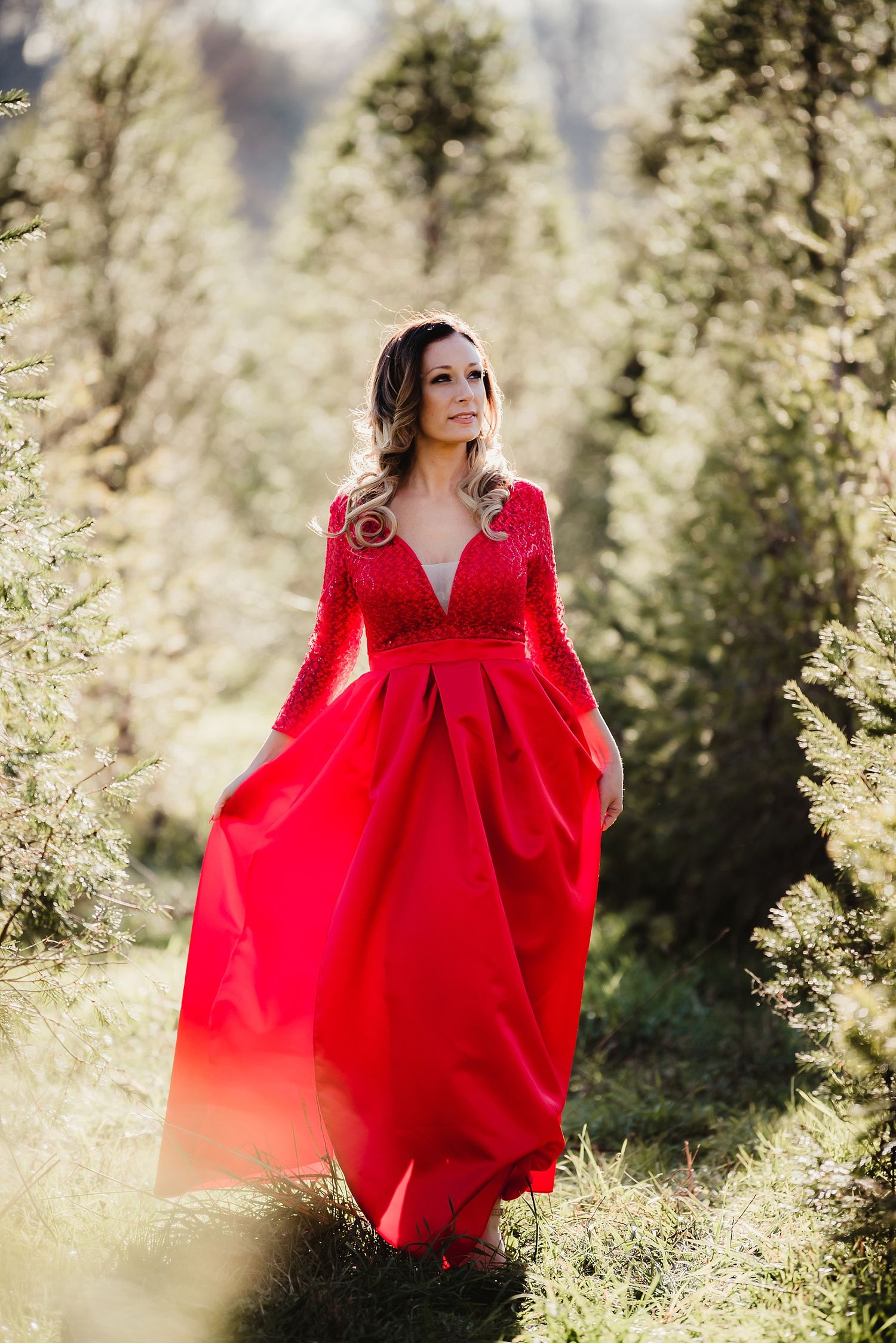 Stunning red ballgown flows in the mountain breeze among evergreen trees.