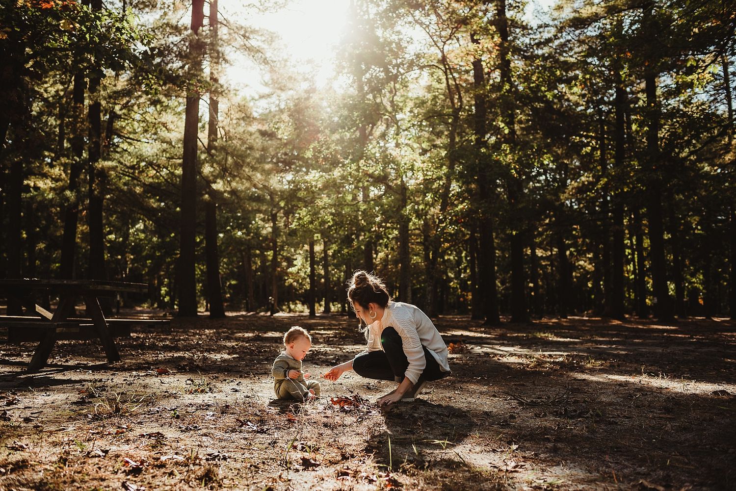 Person crouching in sunlit forest clearing during golden hour.