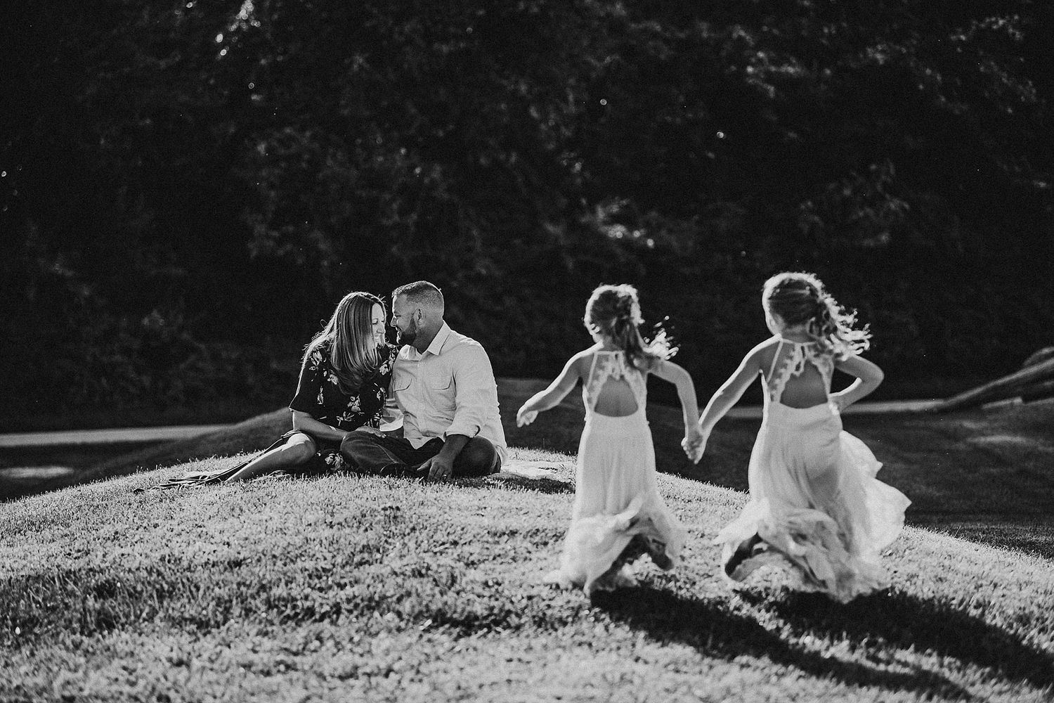 A playful black and white photo of a group running together on a grassy hillside.