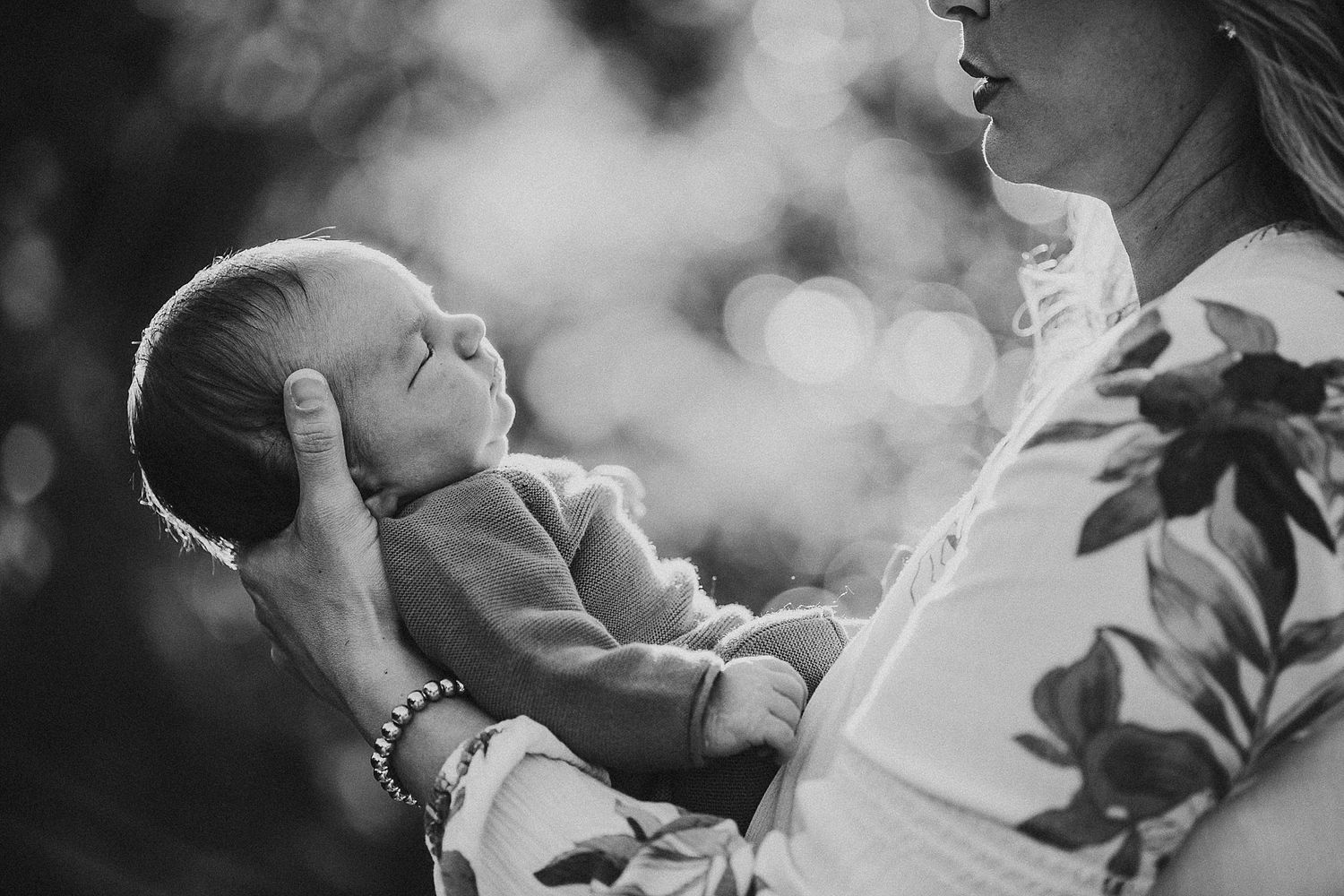 A black and white portrait of a tender moment between parent and infant in soft light.