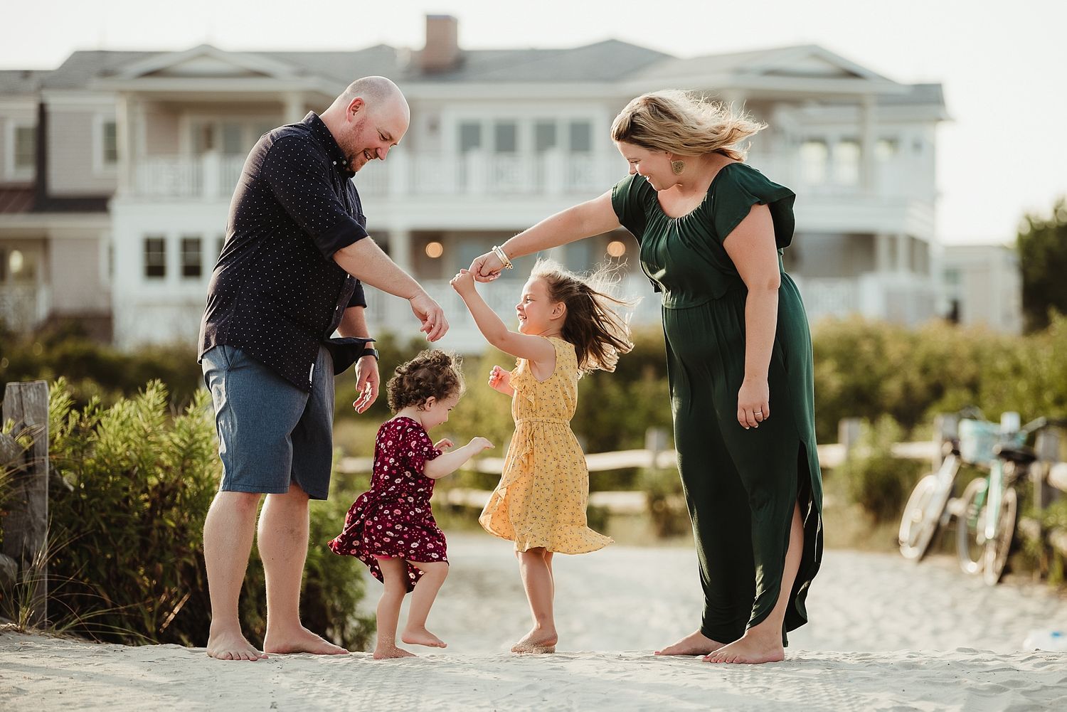 A family playing together on a sandy beach with a large house in the background.