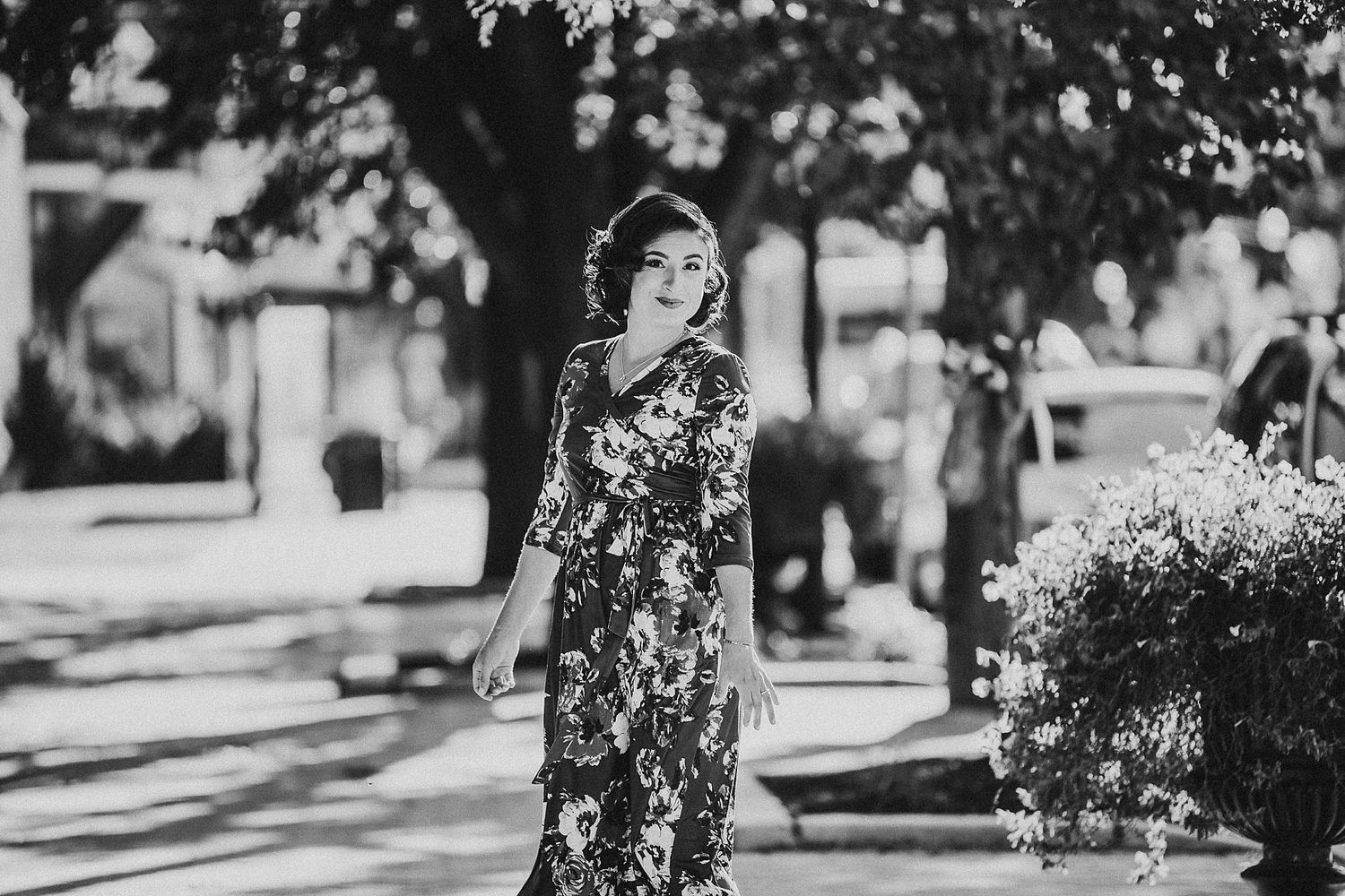 Woman in floral dress standing outdoors on a sunny day with trees in background.