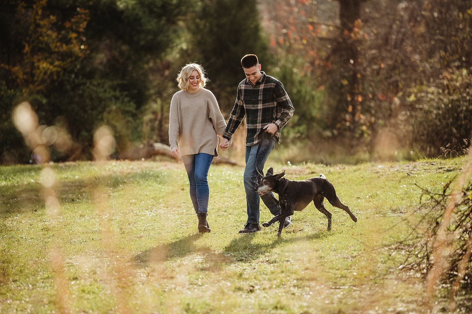 Couple walking their black dog on autumn trail through nature.
