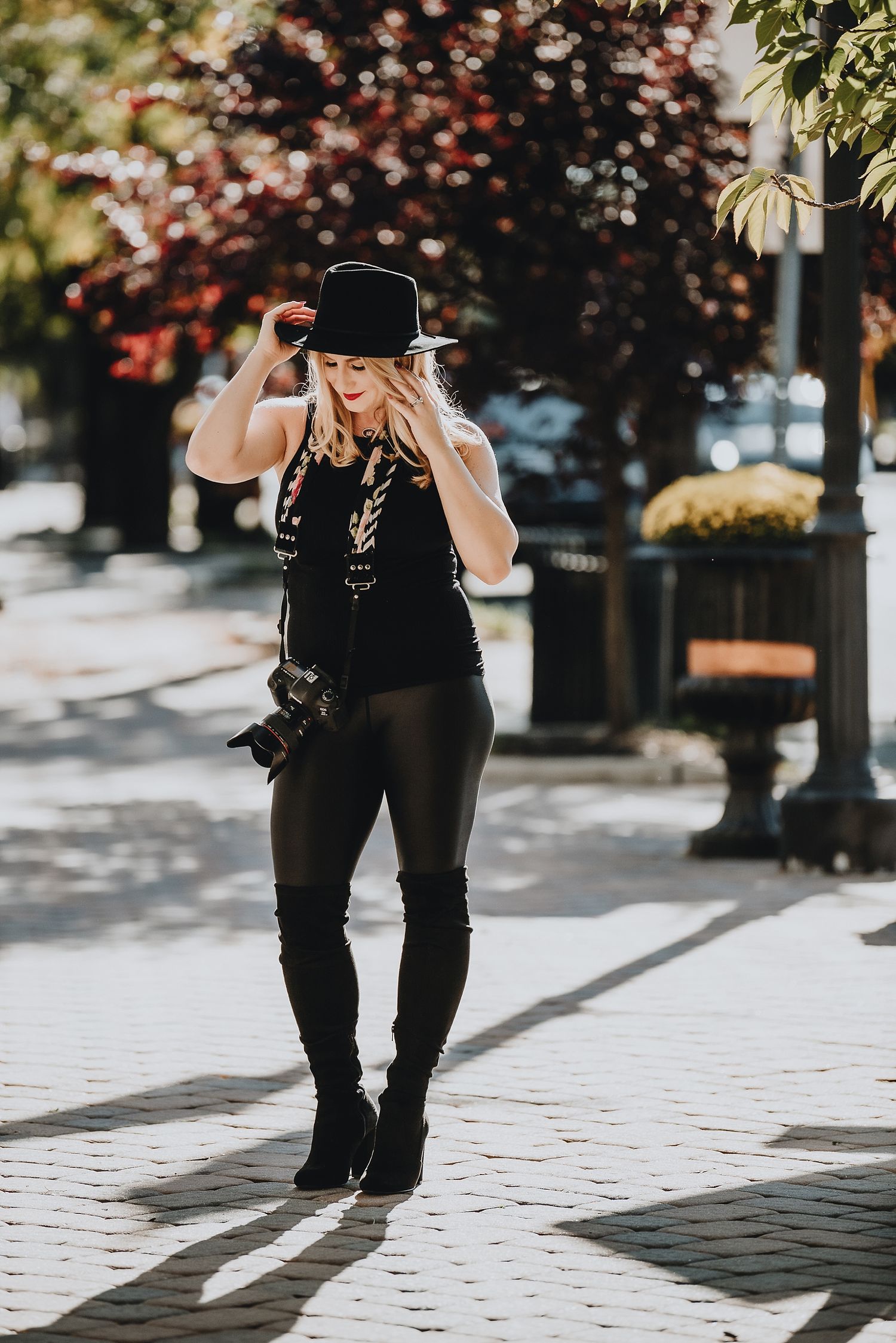 Photographer in black hat and outfit taking pictures on brick sidewalk.