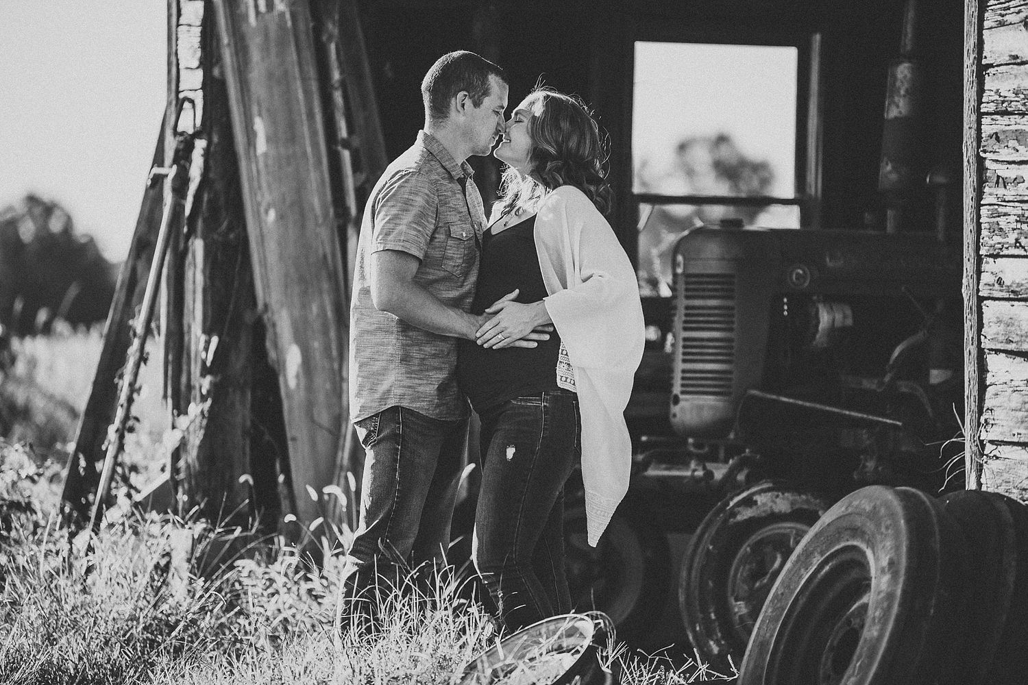 Black and white romantic portrait of couple embracing by vintage tractor.