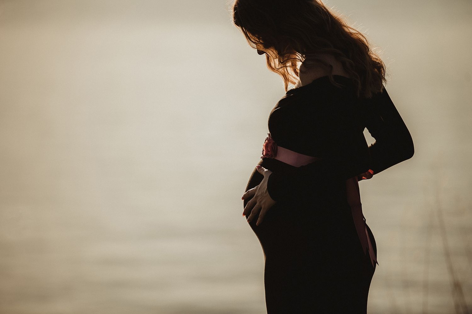 Silhouette of pregnant woman in profile against light background.
