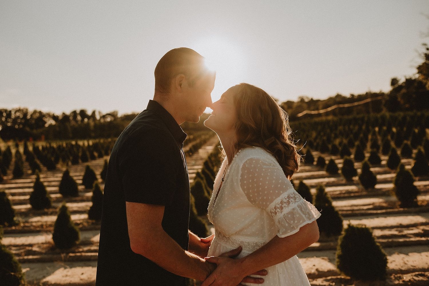 Couple sharing intimate moment at sunset in Christmas tree farm.