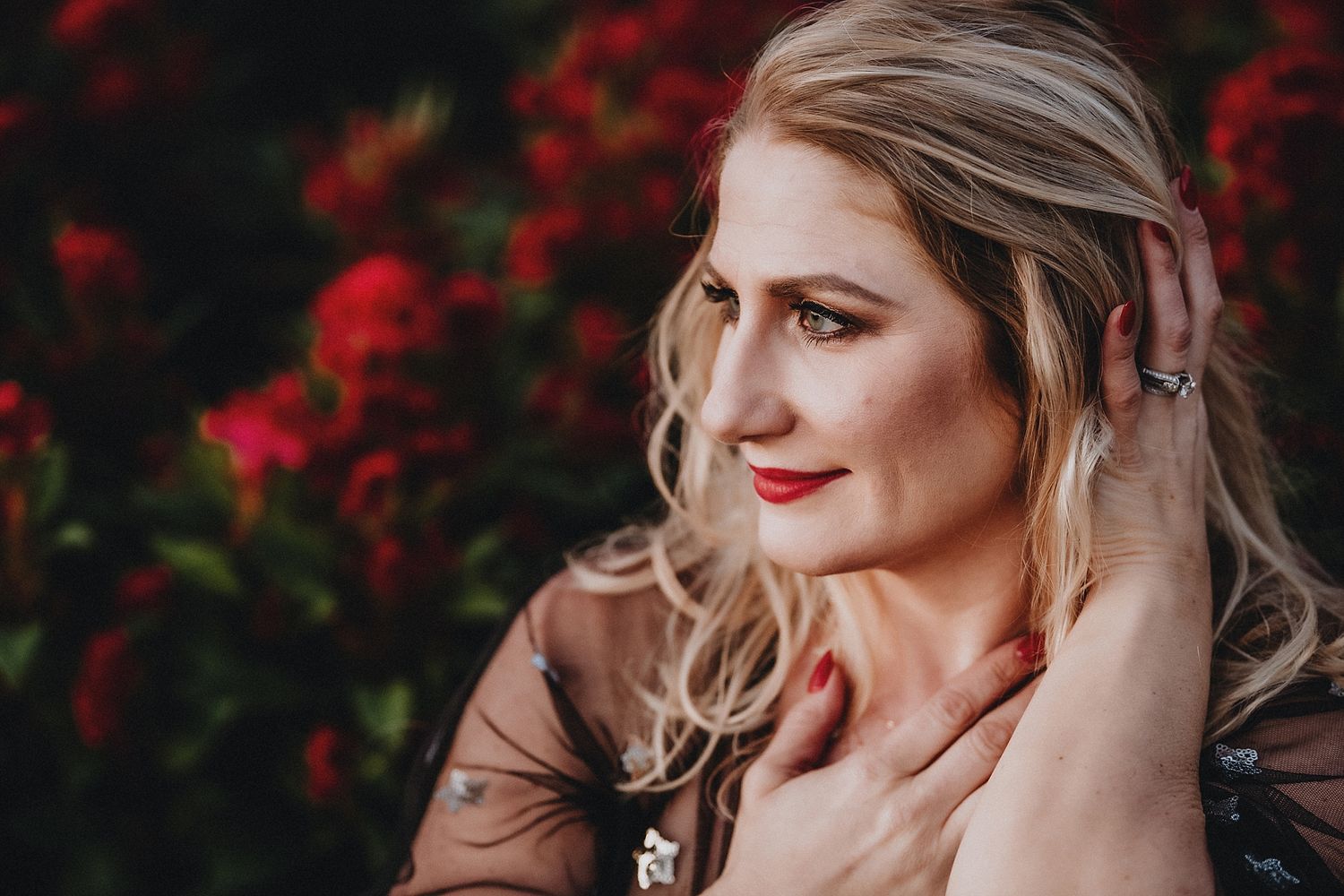 Portrait against red flowers with soft natural lighting and warm tones.