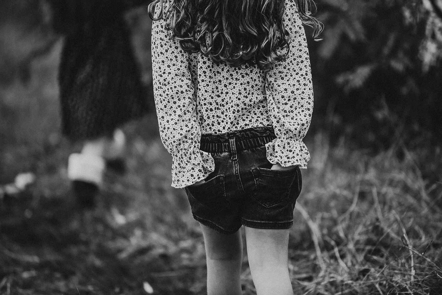 Back view of person wearing polka dot shirt and denim shorts standing in grass.