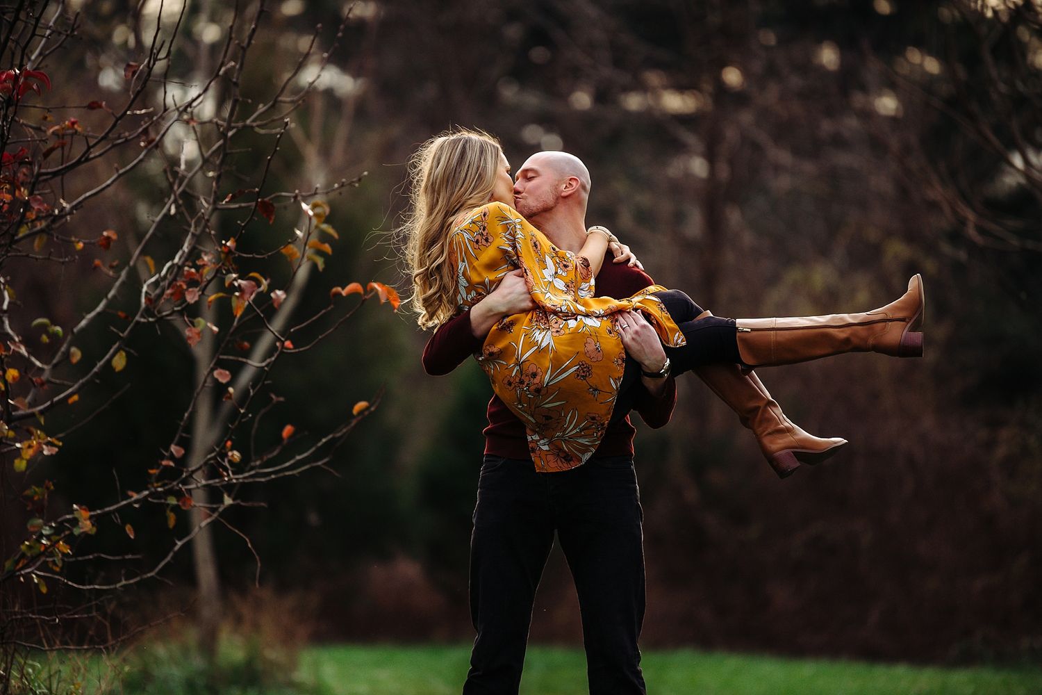 Playful moment captured as couple embraces in autumn garden with golden light filtering through.