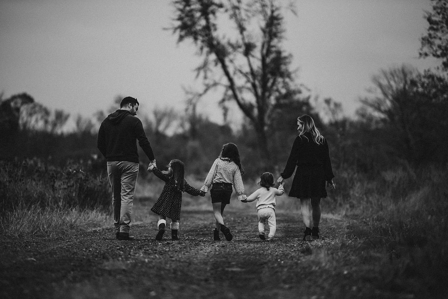Family walking together hand in hand on nature path in black and white photograph.