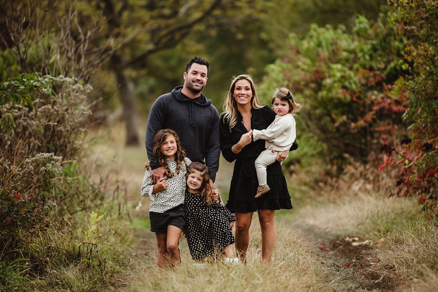 Family of five posing together on an autumn trail surrounded by fall foliage.