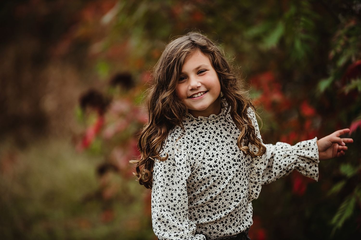 Young child in leopard print top twirling outdoors with autumn foliage in background.